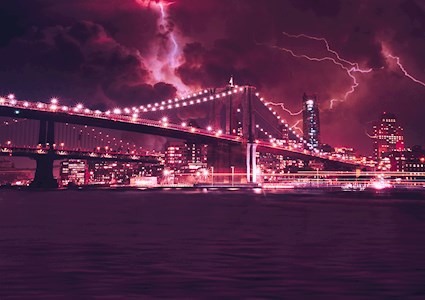 The photograph depicts a large suspension bridge, illuminated at night against an urban skyline, during a lightning storm.